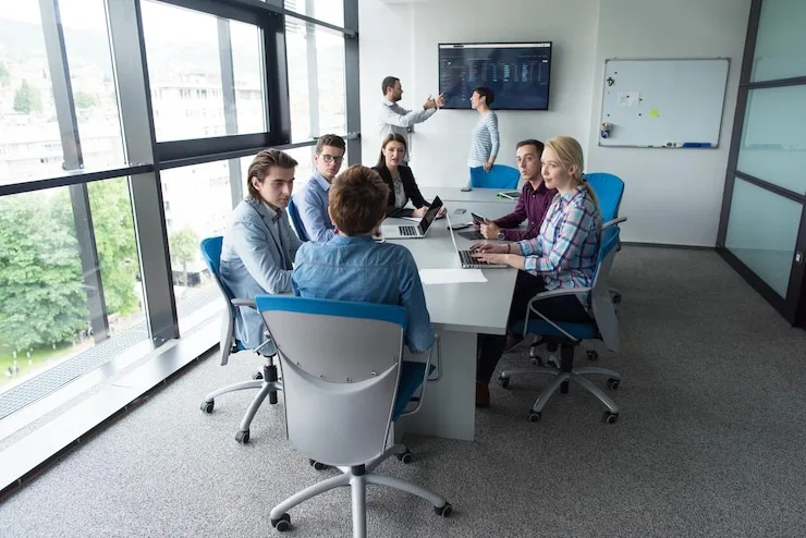 Team seated at a long table in a glass-walled meeting room