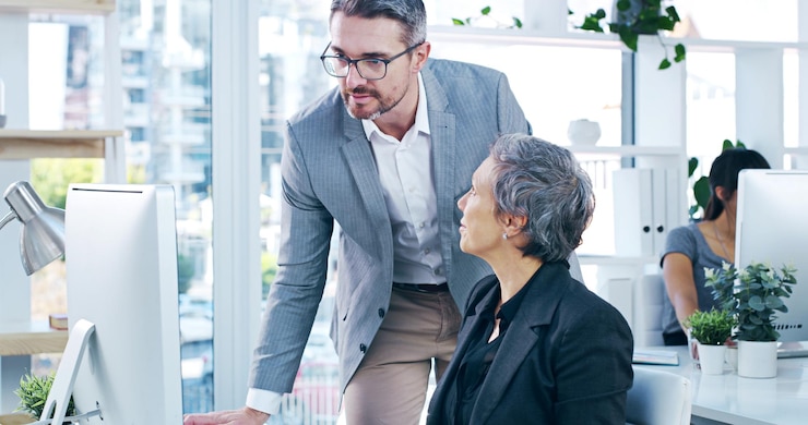 Two colleagues talking at a desk in a bright open-plan office