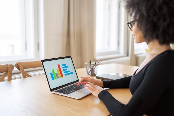 Woman at a wooden table using a laptop that shows a bar chart