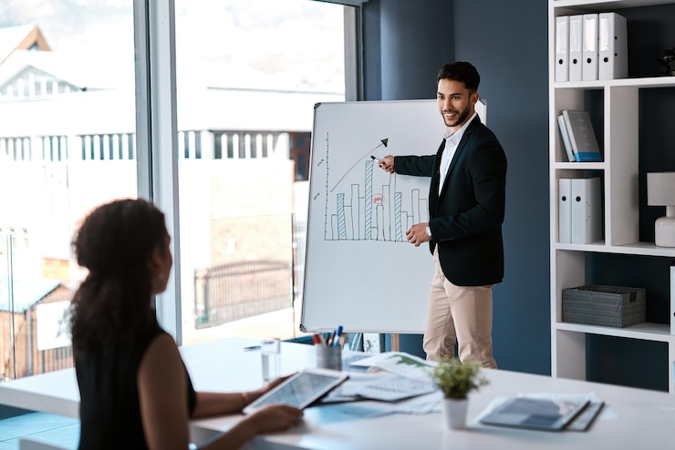 Presenter at a whiteboard with a chart while a colleague takes notes